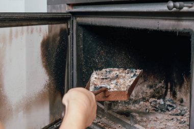Şömine temizliği. Yanmış bir şöminede kürekle kürek tutan bir kadın..