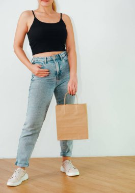 İsrafsız konsept. Eko konsepti. Mavi kotlu ve siyah bluzlu çekici bir kız elinde bir kese kağıdı tutuyor. Plastik poşetleri yasakla. Kesilmiş fotoğraf.