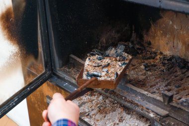 Şömineden kül çıkarma. Ekose gömlekli bir adamın eli şöminenin külleriyle dolu bir kürek tutar..