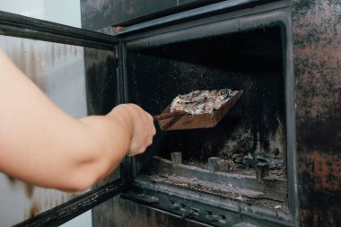 Şömine temizliği. Yanmış bir şöminede kürekle kürek tutan bir kadın..