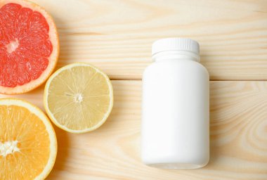 Vitamin modellemesi. Turunçgillerin arka planında vitamin için beyaz boş bir şişe. lemon. Turuncu. Greyfurt. Ahşap arkaplan