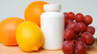Vitaminler. Meyve arkaplanındaki vitaminler için beyaz bir kap. Citrus, limon, portakal, üzüm.