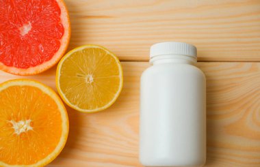 Vitamin modellemesi. Turunçgillerin arka planında vitamin için beyaz boş bir şişe. lemon. Turuncu. Greyfurt. Ahşap arkaplan