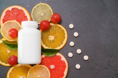 Vitaminler. Turunçgillerin arka planında vitamin için beyaz boş bir şişe. Gri taş arka plan. Boş ilaç şişesi.