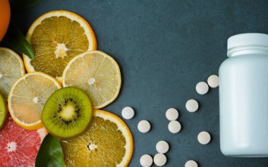 Vitaminler. Turunçgillerin arka planında vitamin için beyaz boş bir şişe. Gri taş arka plan. Boş ilaç şişesi.