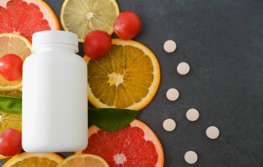Vitaminler. Turunçgillerin arka planında vitamin için beyaz boş bir şişe. Gri taş arka plan. Boş ilaç şişesi.
