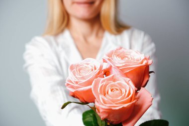 Beyaz gömlekli kadın ellerinde pembe gül çiçeği tutuyor. Çiçeğe yakın görünüm.