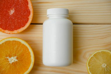 Vitamin modellemesi. Turunçgillerin arka planında vitamin için beyaz boş bir şişe. lemon. Turuncu. Greyfurt. Ahşap arkaplan