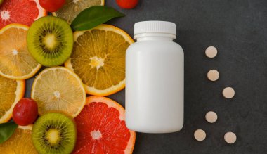 Vitaminler. Turunçgillerin arka planında vitamin için beyaz boş bir şişe. Gri taş arka plan. Boş ilaç şişesi.