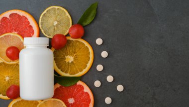 Vitaminler. Turunçgillerin arka planında vitamin için beyaz boş bir şişe. Gri taş arka plan. Boş ilaç şişesi.