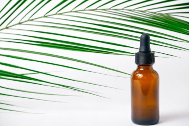 Beyaz arka planda gerekli yağlar, palmiye yaprakları, maketler. Kahverengi cam şişelerde pipetli kozmetik tıbbi güzellik ürünü.