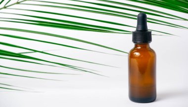 Beyaz arka planda gerekli yağlar, palmiye yaprakları, maketler. Kahverengi cam şişelerde pipetli kozmetik tıbbi güzellik ürünü.