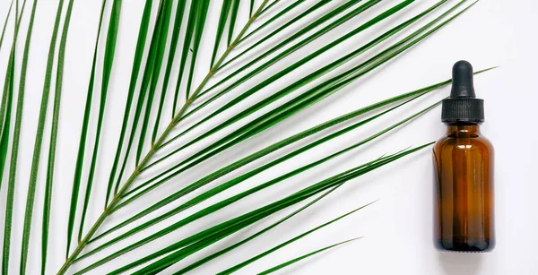 Beyaz arka planda gerekli yağlar, palmiye yaprakları, maketler. Kahverengi cam şişelerde pipetli kozmetik tıbbi güzellik ürünü.