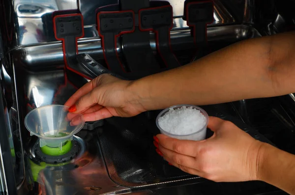 Adding salt to the dishwasher. A woman\'s hand pours salt to soften the water into the dishwasher.