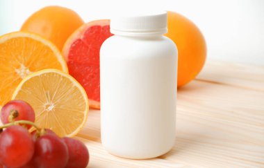 Hap mı vitamin mi? Ahşap bir masada vitamin için beyaz boş bir şişe. Sulu narenciye dilimleri. lemon. Turuncu. Greyfurt. Üzüm.