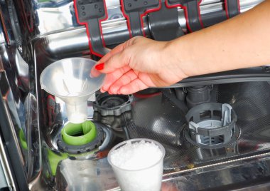Bulaşık makinesine tuz ekliyorum. Bir kadının eli, suyu bulaşık makinesine yumuşatmak için tuz döküyor..