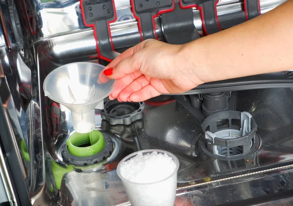 Adding salt to the dishwasher. A woman\'s hand pours salt to soften the water into the dishwasher.