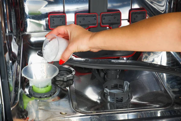 Adding salt to the dishwasher. A woman\'s hand pours salt to soften the water into the dishwasher.