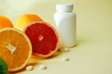 Vitaminler. Tıbbi konsept. Eczane ya da doğal. Vitaminli beyaz şişe, dağınık haplar. Sulu narenciye dilimleri. lemon. Turuncu. Greyfurt.