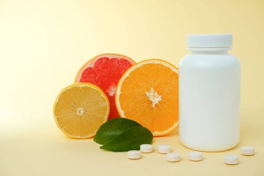 Yiyeceklerden ya da takviye malzemelerinden alınan vitaminler. Beyaz plastik şişeden dökülen vitamin tableti taze portakal meyveleri ve yeşil yaprak. Sağlıklı yaşam için doğal takviyeler