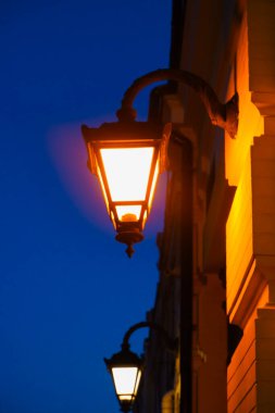 Retro lantern with yellow warm light on the facade of the building. Street lights, illumination. Twilight on the street of the old city. Old lamp glows in the evening