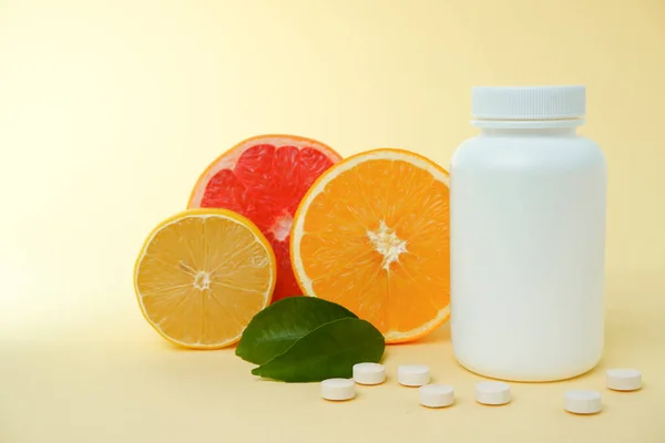 Vitamins from foods or supplements choices. Vitamin tablet spilling out of white plastic bottle with fresh juicy orange fruits and green leaf. natural supplements for healthy good life