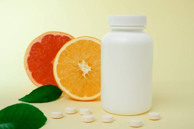 Yiyeceklerden ya da takviye malzemelerinden alınan vitaminler. Beyaz plastik şişeden dökülen vitamin tableti taze portakal meyveleri ve yeşil yaprak. Sağlıklı yaşam için doğal takviyeler