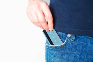 Genç bir adam kot pantolonunun cebinden kredi kartını çıkardı. Bir elde yakın plan, açık arkaplanda pantolondan ödeme kartı çıkartırken..