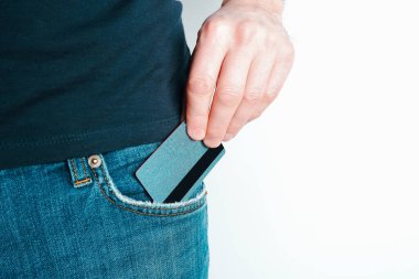 Genç bir adam kot pantolonunun cebinden kredi kartını çıkardı. Bir elde yakın plan, açık arkaplanda pantolondan ödeme kartı çıkartırken..