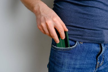 Genç bir adam kot pantolonunun cebinden kredi kartını çıkardı. Bir elde yakın plan, açık arkaplanda pantolondan ödeme kartı çıkartırken..