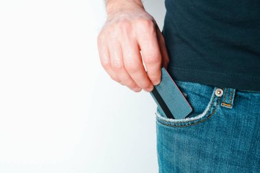 Genç bir adam kot pantolonunun cebinden kredi kartını çıkardı. Bir elde yakın plan, açık arkaplanda pantolondan ödeme kartı çıkartırken..