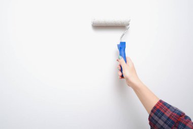 Resim işe yarıyor. Bir kadın boya silindiriyle ışık duvarı boyuyor. Bir araçla bir ele yakın çekim.