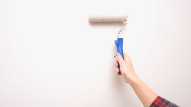 Resim işe yarıyor. Bir kadın boya silindiriyle ışık duvarı boyuyor. Bir araçla bir ele yakın çekim.