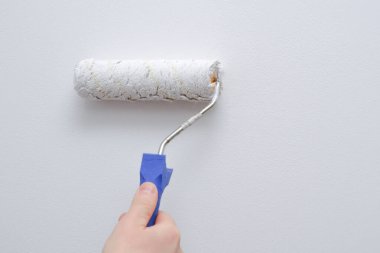 Resim işe yarıyor. Bir adam boya silindiriyle ışık duvarı boyuyor. Bir araçla bir ele yakın çekim.