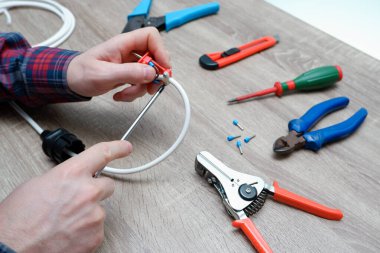 Erkek bir elektrikçi elektrik kablosunun fişini değiştiriyor. Elektrikli aletlerle çalışmak. Striptizci, kötürüm, tornavida, tel kesici..