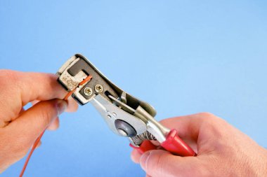 Bir elektrikçi bakır bir kablodan yalıtımı kaldırır. Aletle çalışmak. Striptizci işi..
