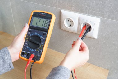 Çoklu metresi olan bir kadın elektrik şebekesinin voltajını kontrol ediyor. Ellerin yakın görüntüsü ve soketin yanındaki alet..