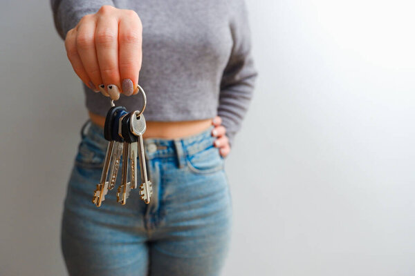 An attractive woman in jeans and a top holds out a bunch of keys in her hand. People lifestyle concept. copy space. Hold house bunch of keys, pointing index finger aside.