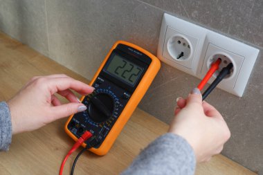 Çoklu metresi olan bir kadın elektrik şebekesinin voltajını kontrol ediyor. Ellerin yakın görüntüsü ve soketin yanındaki alet..