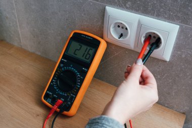 Çoklu metresi olan bir kadın elektrik şebekesinin voltajını kontrol ediyor. Ellerin yakın görüntüsü ve soketin yanındaki alet..
