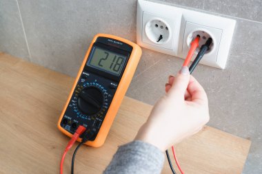 Çoklu metresi olan bir kadın elektrik şebekesinin voltajını kontrol ediyor. Ellerin yakın görüntüsü ve soketin yanındaki alet..