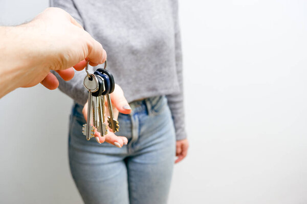 Focus on female hand holding house keys. Woman realtor giving bunch to new happy owner of property. Holding in hands house and bunch of keys. People lifestyle concept.