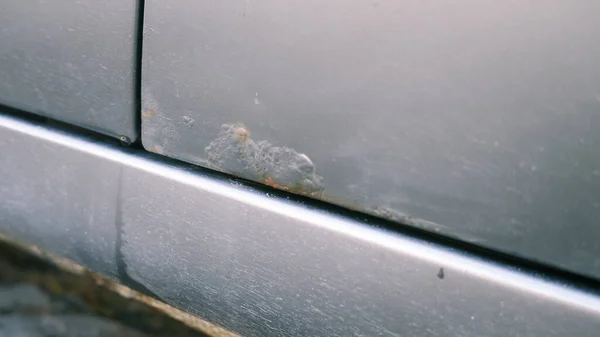 Close-up, selective focus on rust and hand. A man shows rust on a car door from winter reagents.