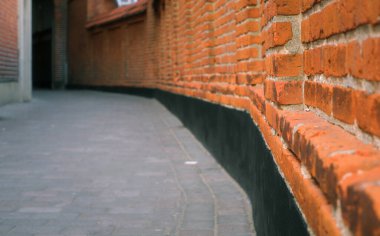 Kırmızı tuğla duvarlarla çevrili dar bir yol. Gündüz perspektifte iki kırmızı tuğla duvar arasında dar bir ara sokak.