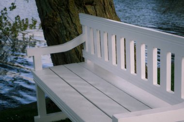 White painted wooden bench on the shore of the lake in the city park.