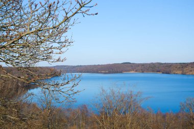 Peyzaj suyu, güzel bahar manzarası. Açık bir bahar gününde, yuvarlanan kırsal bölgenin Mavi Gölü. Bahar, ön planda tomurcukları olan büyük bir ağacın dalları..