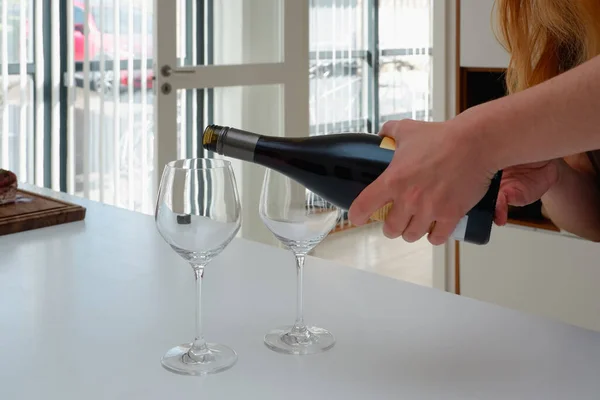 A woman pours red wine from a bottle into wine glasses. Modern white kitchen clean interior design. Glass of wine in female hand.