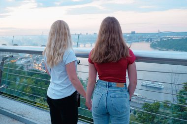 Gözlem masasındaki iki genç kız Kiev, Ukrayna 'nın merkezindeki Dinyeper nehrine bakıyor, hava manzaralı. Arkadan bak. Dişiler şehre bakıyor..