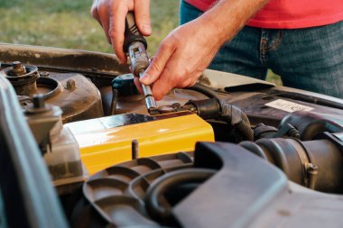 Tamirci, eski bir arabanın aküsünü değiştiriyor. Bir adam yeni pil takmak, yedek parça takmak için İngiliz anahtarı cıvatalarıyla sıkıyor.