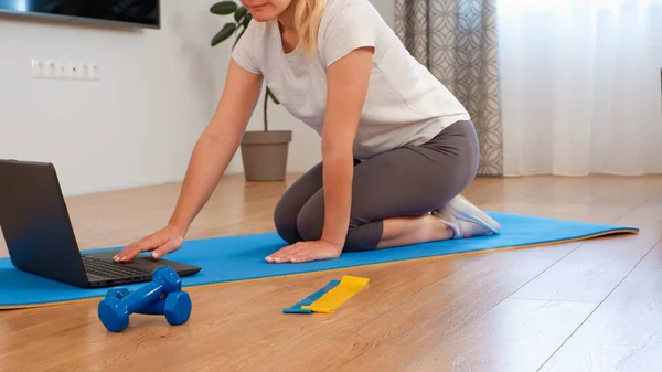 Home workout with laptop and work at home concept. Fitness woman watching online lesson at laptop and exercising with a fitness rubber band indoors. caucasian sporty woman having online fitness class at home.